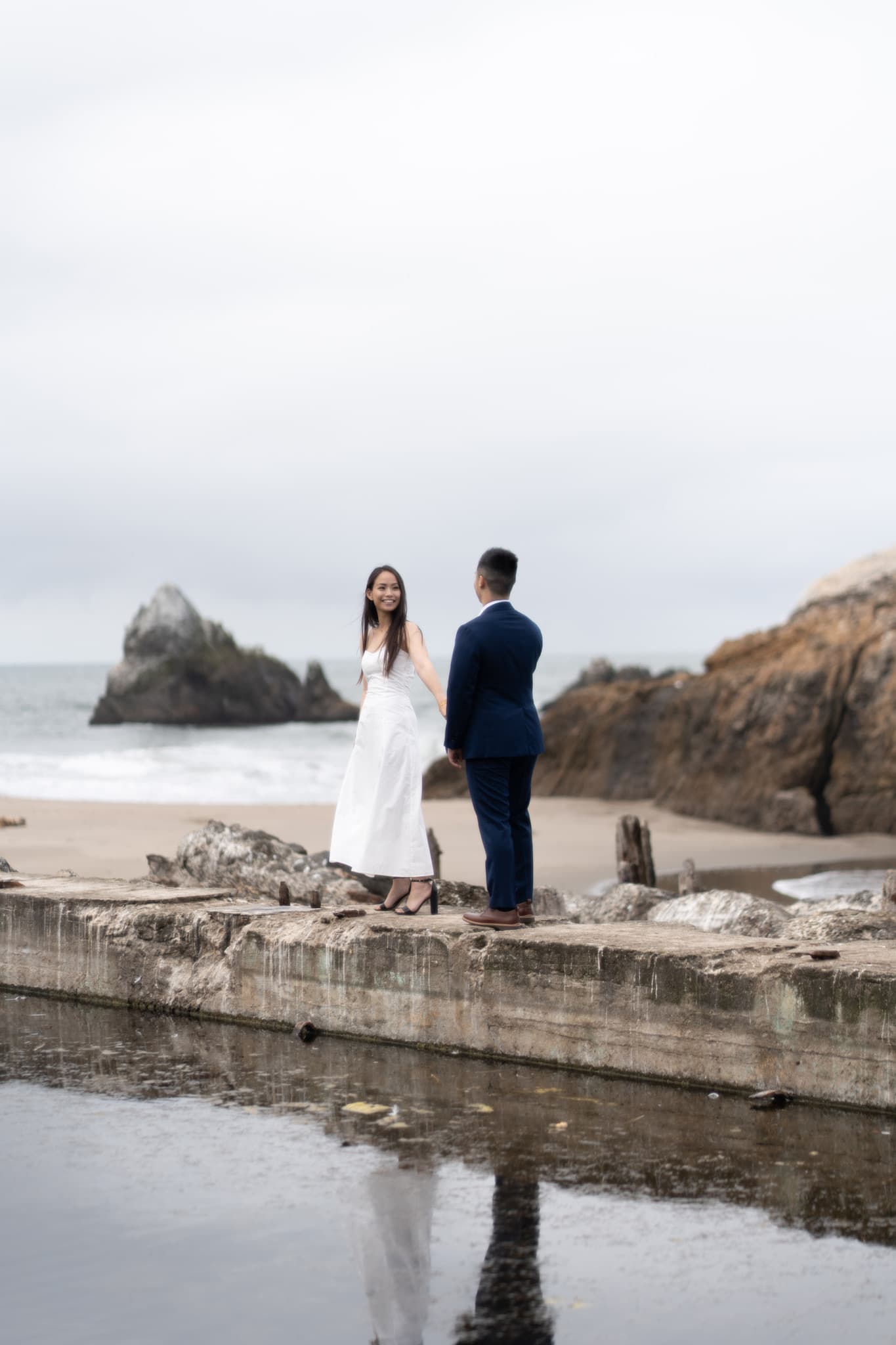 Bride and groom on the rocks on a cloudy day by the sea